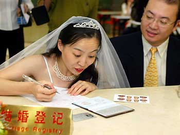 A woman fills in the marriage registration form as her fiance looks on at a registry in Shanghai on October 1, 2003. The revised Marriage Law took effect on the day. [newsphoto/file]